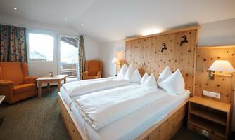 A cozy hotel room with two single beds and decorative cushions. The warm wood paneling and large windows create an inviting atmosphere.