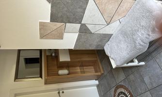 A modern entrance area with a tiled floor and a wooden shelf. Decorative tiles in various colors are mounted on the wall.