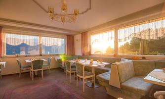 A cozy dining room with tables and chairs. The sunlight streams through the windows, creating an inviting atmosphere.