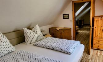 A cozy bedroom with two single beds and bright bedding. The room features wooden furniture and a slightly sloping roof.