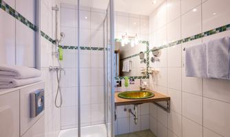 A modern bathroom with a shower and colorful sink. The walls are tiled and the room is well lit.
