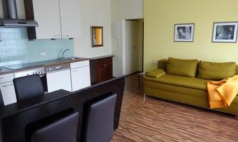 A modern apartment with an open kitchen and a cozy living area. The walls are painted in a light yellow, and a sofa with a blanket is ready.