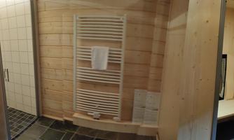 A modern bathroom with wood paneling and a towel radiator. The floor is designed with dark tiles.