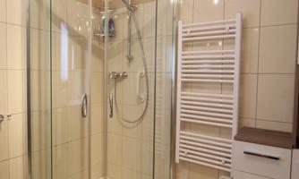 A modern bathroom with a glass shower and bright tiles. There is also a towel radiator and a small storage space.