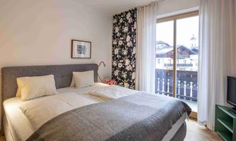 A cozy bedroom with a large bed and bright pillows. The balcony offers a view of the landscape and windows with curtains.