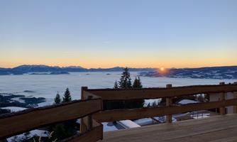 A beautiful view of a snow-covered landscape with a sunset on the horizon. The sight extends over a sea of clouds to the mountains in the background.