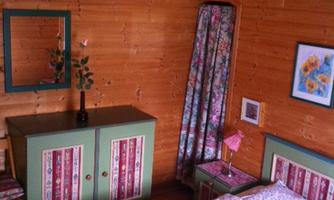 A cozy room with wooden walls, a bed, and colorful furniture. There is a floral pattern on the floor.