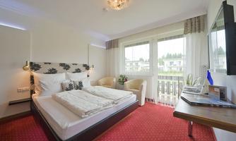 A cozy bedroom with a large bed and modern furniture. Large windows offer a view of the surroundings and plenty of natural light.