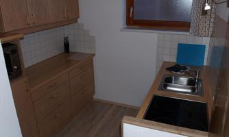 A small kitchen with wooden cabinets and a sink. The room is bright and has a window that lets in natural light.