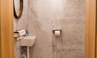 A modern bathroom with gray tiles and a white toilet. A round mirror is hanging on the wall and there is a towel rack.