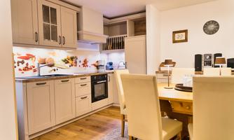 A modern kitchen with bright furniture and a cozy dining area. The cooking surface is well equipped and decoratively designed.