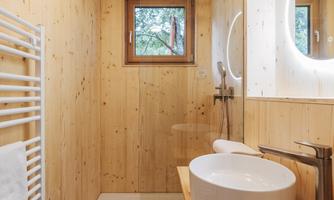 A modern bathroom with wood paneling and a large shower. The room is bright and designed in a minimalist style, featuring a round sink on a wooden countertop.