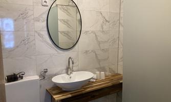 A modern bathroom with marble tiles and a round mirror surface. The wooden shelf and the washbasin give the room a stylish touch.