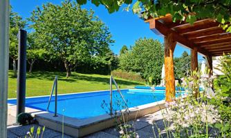 A beautiful pool surrounded by green grass and trees. In the background, a blue sky can be seen.