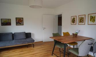 A bright and modern living room with a gray sofa and a wooden table. Some pictures are hanging on the walls, and the floor is made of wood.