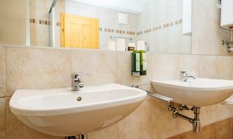 A modern bathroom with two sinks and clear, elegant lines. In the background, wooden details and large mirrors can be seen.