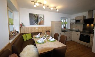 A modern kitchen with an elegant dining table and cozy seating. A picture of an animal hangs on the wall, and the windows are decorated with green curtains.