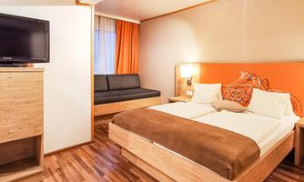 A modern bedroom with wooden flooring and a cozy atmosphere. The room features a double bed, a couch, and a television.