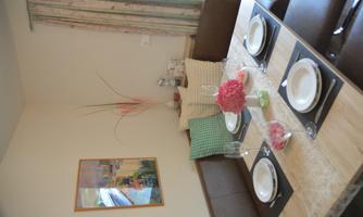 An inviting dining area with a wooden table, beautifully set with dishes and glasses. The walls are adorned with a piece of artwork and curtains in a soft pattern.