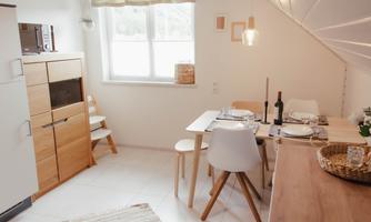 A modern kitchen corner with a dining table, chairs, and bright furniture. The environment is friendly and inviting, with natural light.