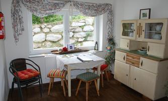 A cozy dining area with a table, chairs, and a sideboard. Through the window, you can see a garden with stones.
