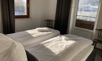 A cozy bedroom with two single beds and bright light streaming through the window. In the background, there is a beautiful view of the winter landscape.