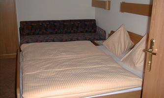 A cozy hotel room with a double bed and a sofa. The walls are painted in neutral colors, and the bedding is in soft shades.