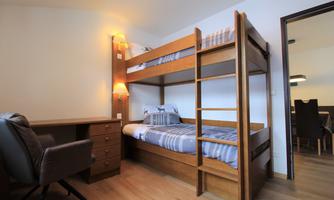 A cozy bedroom with a wooden loft bed and a desk. The room is bright and furnished in a modern style.