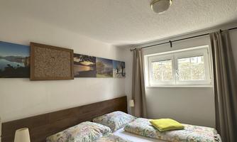 A cozy bedroom with two single beds and colorful bedspreads. Pictures hang on the wall, and the light gently falls through the window.