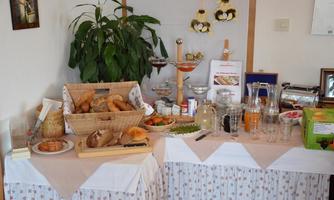 A rich breakfast buffet with fresh rolls, pastries, and various beverages. In the background, there is a large plant and several decorative elements.