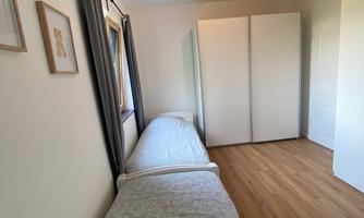 A simple room with two single beds and a large wardrobe. Bright walls and a friendly floor create an inviting atmosphere.