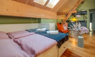 A cozy bedroom with a double bed and wooden details. On the wall, there are plants and a stylish vase with flowers.