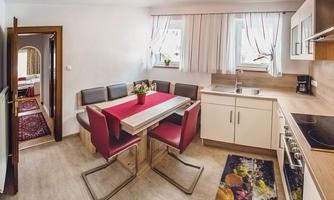 A modern kitchen with a dining table and comfortable red chairs. The room design is bright and inviting.