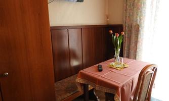 A cozy dining area with a wooden table, a chair, and a vase with tulips. There is a television on the wall and a curtain made of colorful fabric.