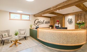 A reception area with warm wooden elements and a modern counter. A smiling employee stands behind the reception desk.