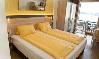 A cozy hotel room with two single beds and yellow bed covers. The view from the window offers a view of the water and a terrace.