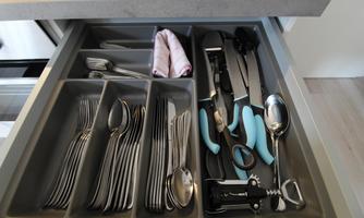 An organized kitchen drawer with cutlery and kitchen tools. The drawer contains spoons, forks, knives, and other utensils.