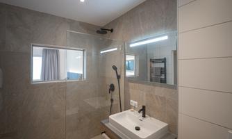A modern bathroom with a large glass shower. The walls are done in light stone, and there is an elegant sink.