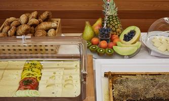 A breakfast buffet with fresh fruit, muesli, and various rolls. The selection also includes honey and cheese.
