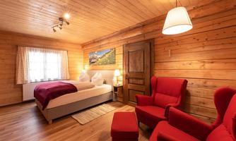 A cozy room with wooden paneling and a large bed. Red armchairs and warm lighting create an inviting atmosphere.