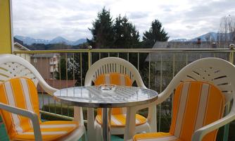 A balcony with a round table and two chairs with an orange and white striped pattern. In the background, mountains and trees can be seen.