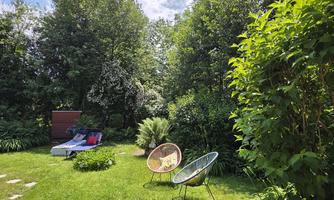 A quiet garden with many trees. There are two cozy chairs and sun loungers.