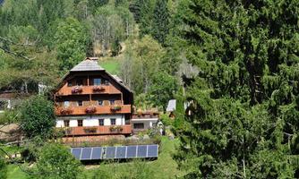 A beautiful house surrounded by trees and green meadows. In the foreground, solar panels can be seen.