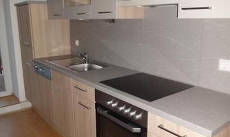A modern kitchen with wooden cabinets and a bright countertop. It features a stove, an oven, and a sink.