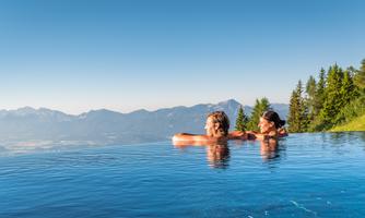 An infinity pool with a view of the mountains. Two people are enjoying the view in the warm sun.