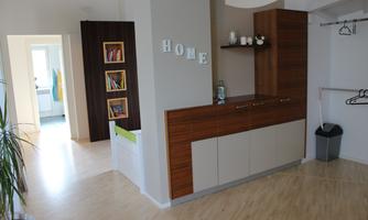 A cozy apartment with a wooden shelf and a modern kitchen element. The rooms are bright and inviting, with a clear view into the hallway.