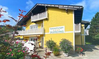 A colorful yellow holiday home with balconies and blooming plants. The entrance is clearly visible and inviting.