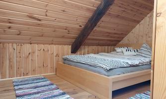 A cozy bedroom in the attic with wooden paneling. The bed is simple and colorful rugs are laid on the floor.