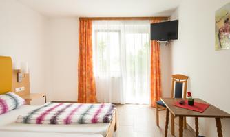 A cozy room with two beds, a table, and a TV. The large windows let in a lot of light and offer a view outside.