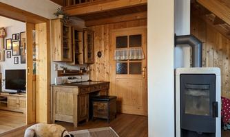 A cozy room with wooden walls and a wood stove. A dog is lying relaxed on a rug in the corner.
